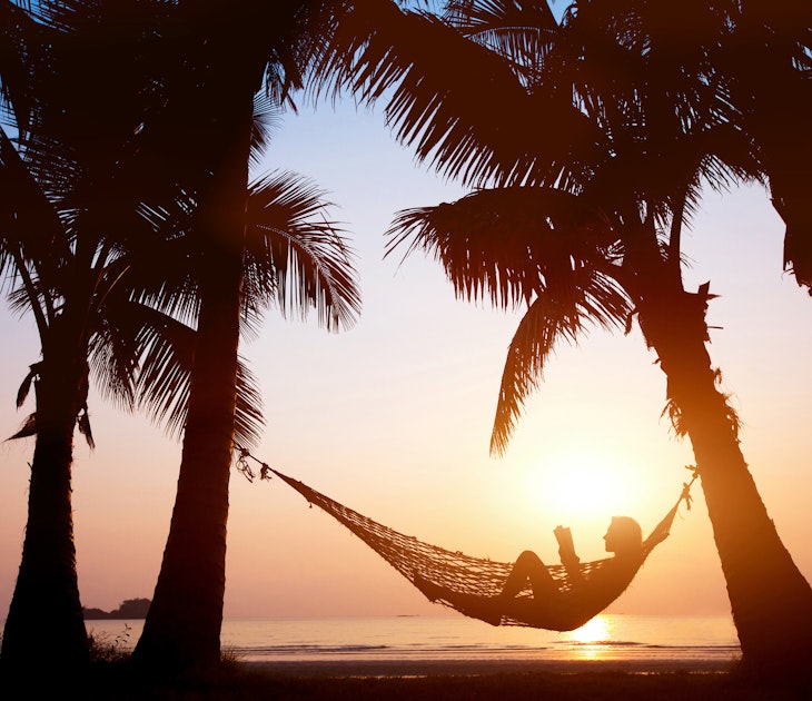 Silhouette of a woman relaxing in a hammock on a beach during sunset.
