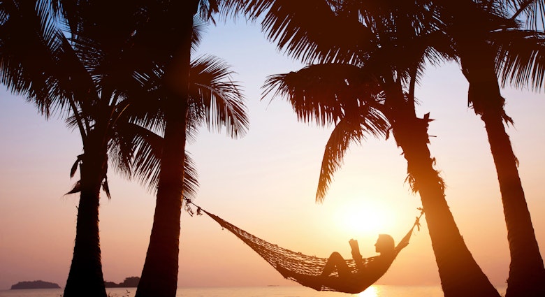 Silhouette of a woman relaxing in a hammock on a beach during sunset.