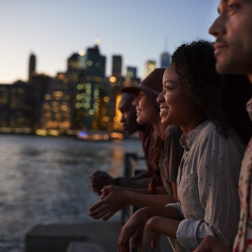 Four people sitting by the river at dusk with the Manhattan skyline beyond.