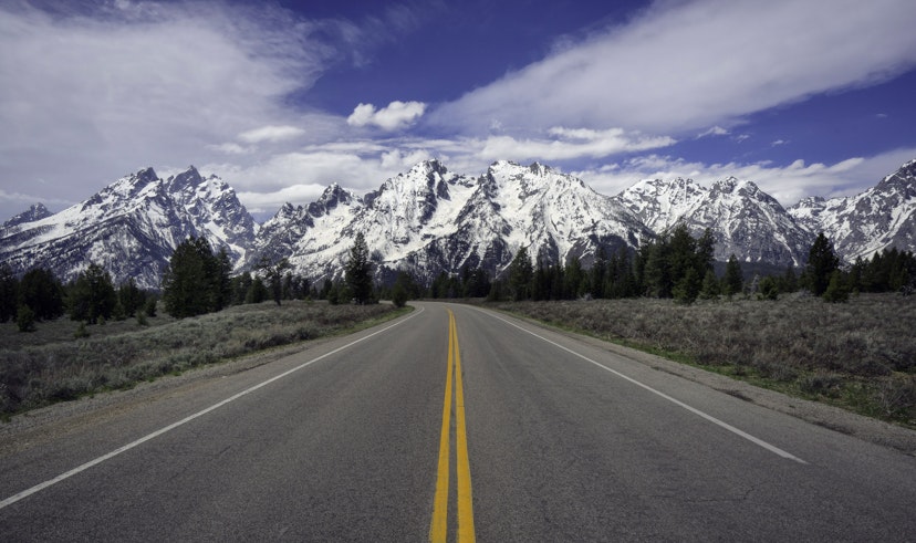 Empty road leading toward the snow-capped mountains in Jackson Hole valley.