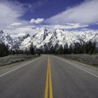Empty road leading toward the snow-capped mountains in Jackson Hole valley.