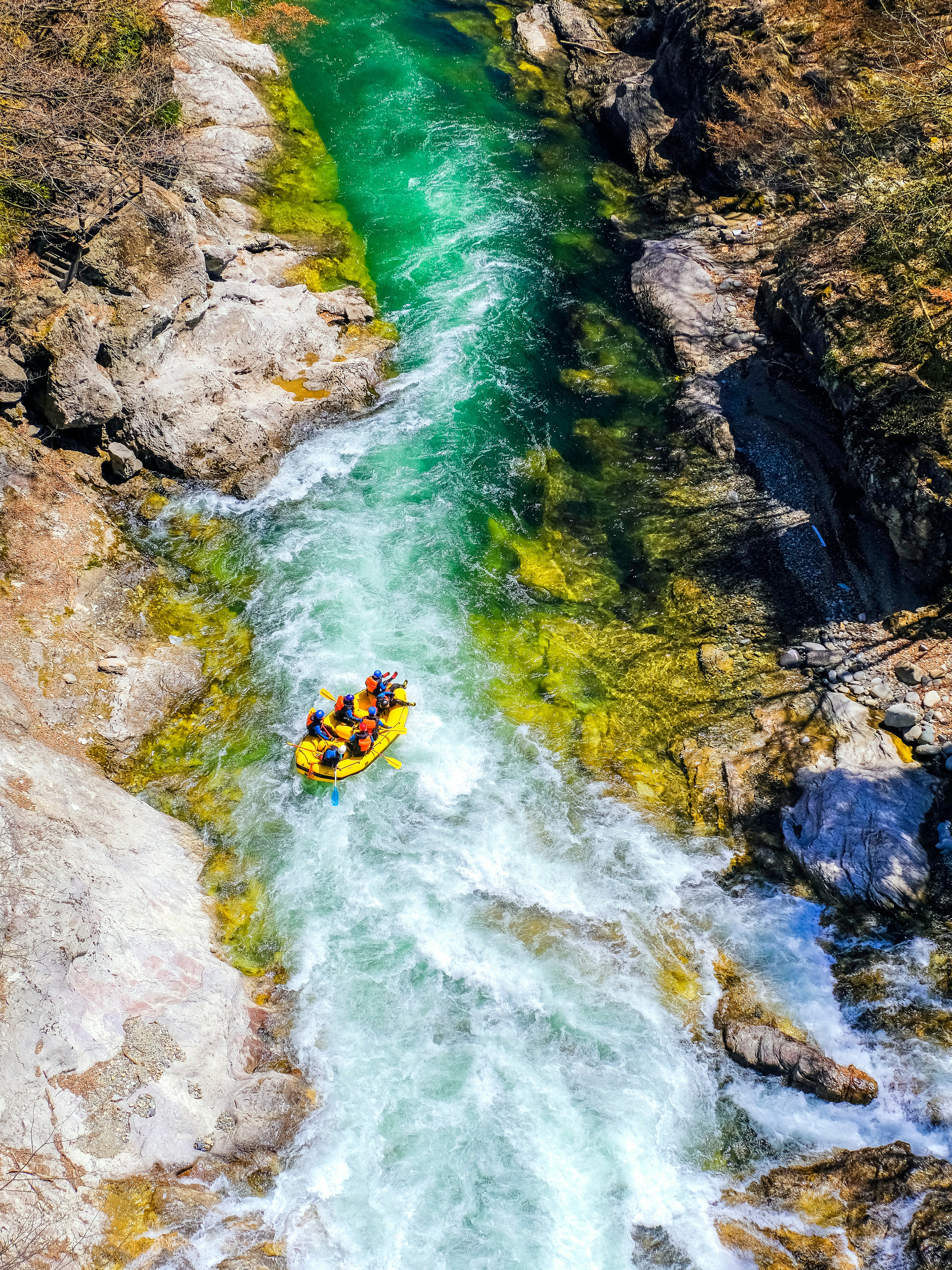 Looking down from above at a group of paddlers riding a raft through a raging river canyon