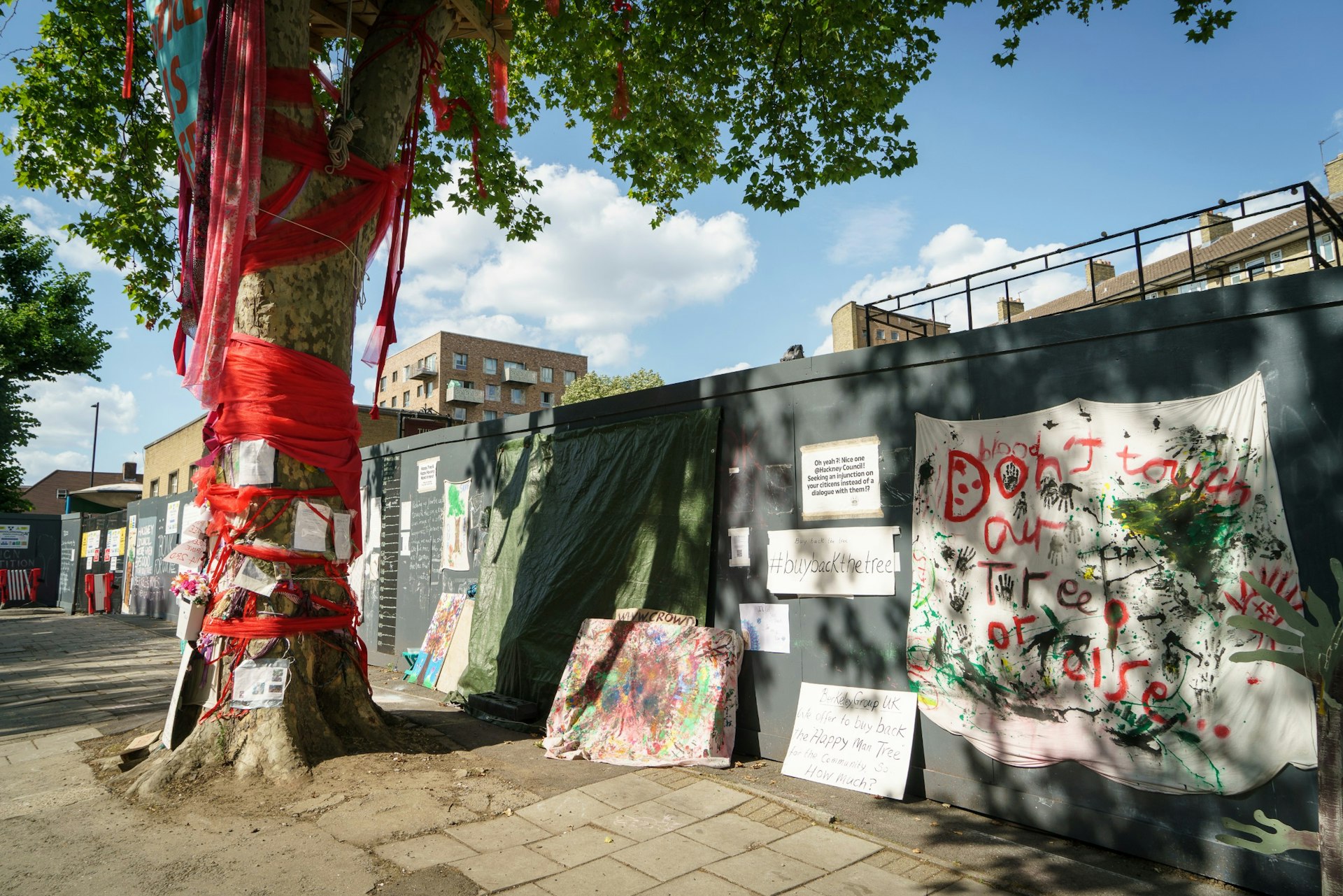 A tree tied with red material and posters urging the saving of the tree