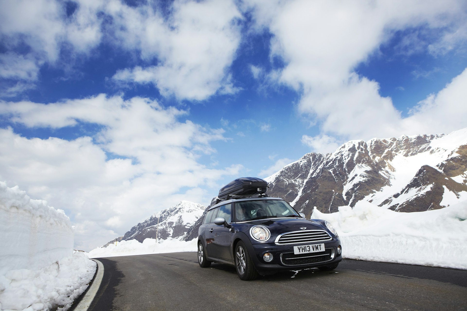 A black Mini drives a mountainous road lined with snow