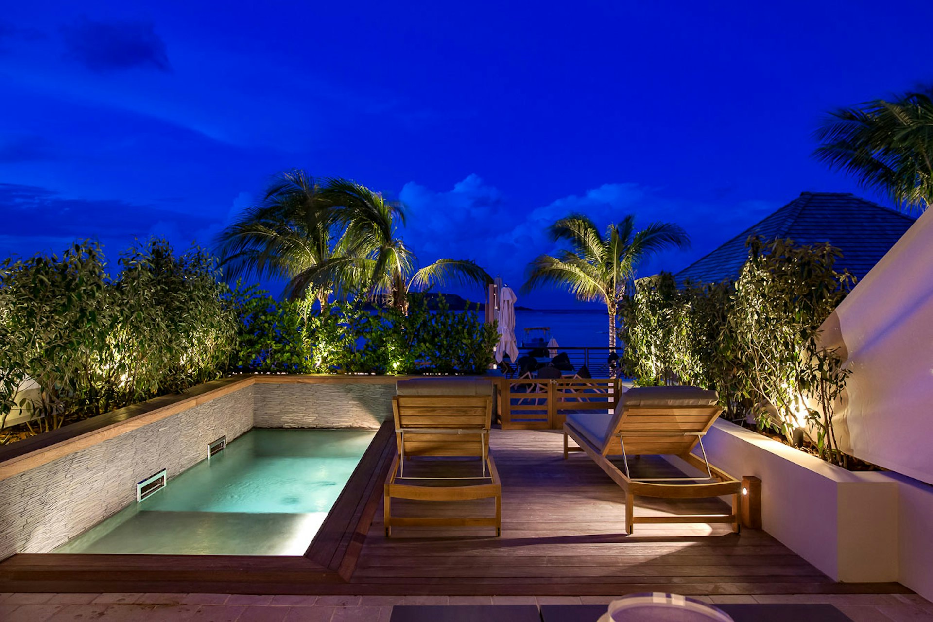 A night shot of a private plunge pool and two empty sunloungers on a deck facing out towards the ocean