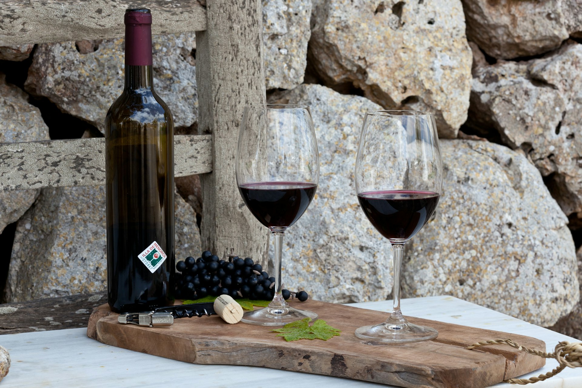 Two glasses of red wine stand next to a wine bottle on a wooden board