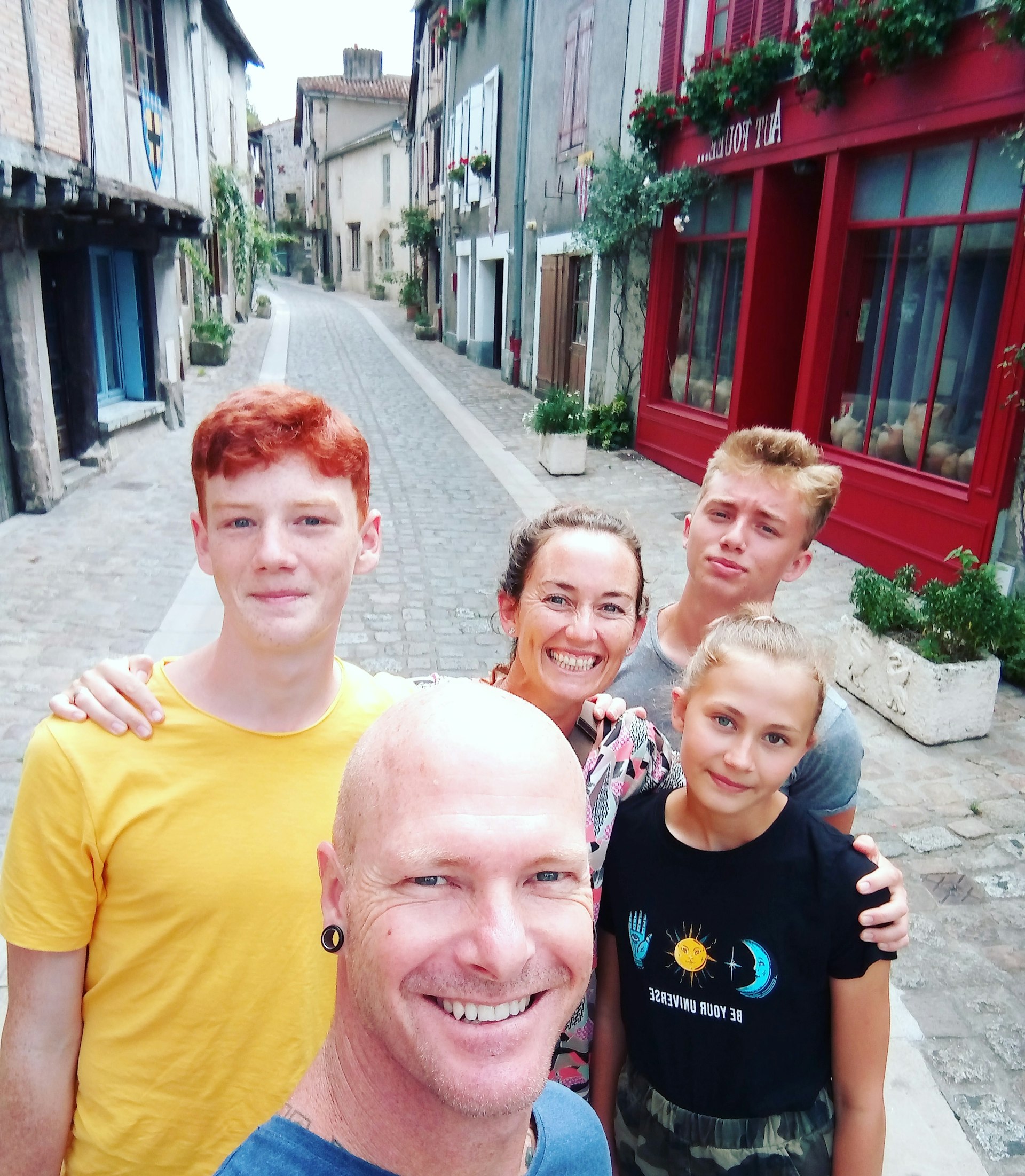 A family of two adults and three children pose for a selfie on a cobbled street