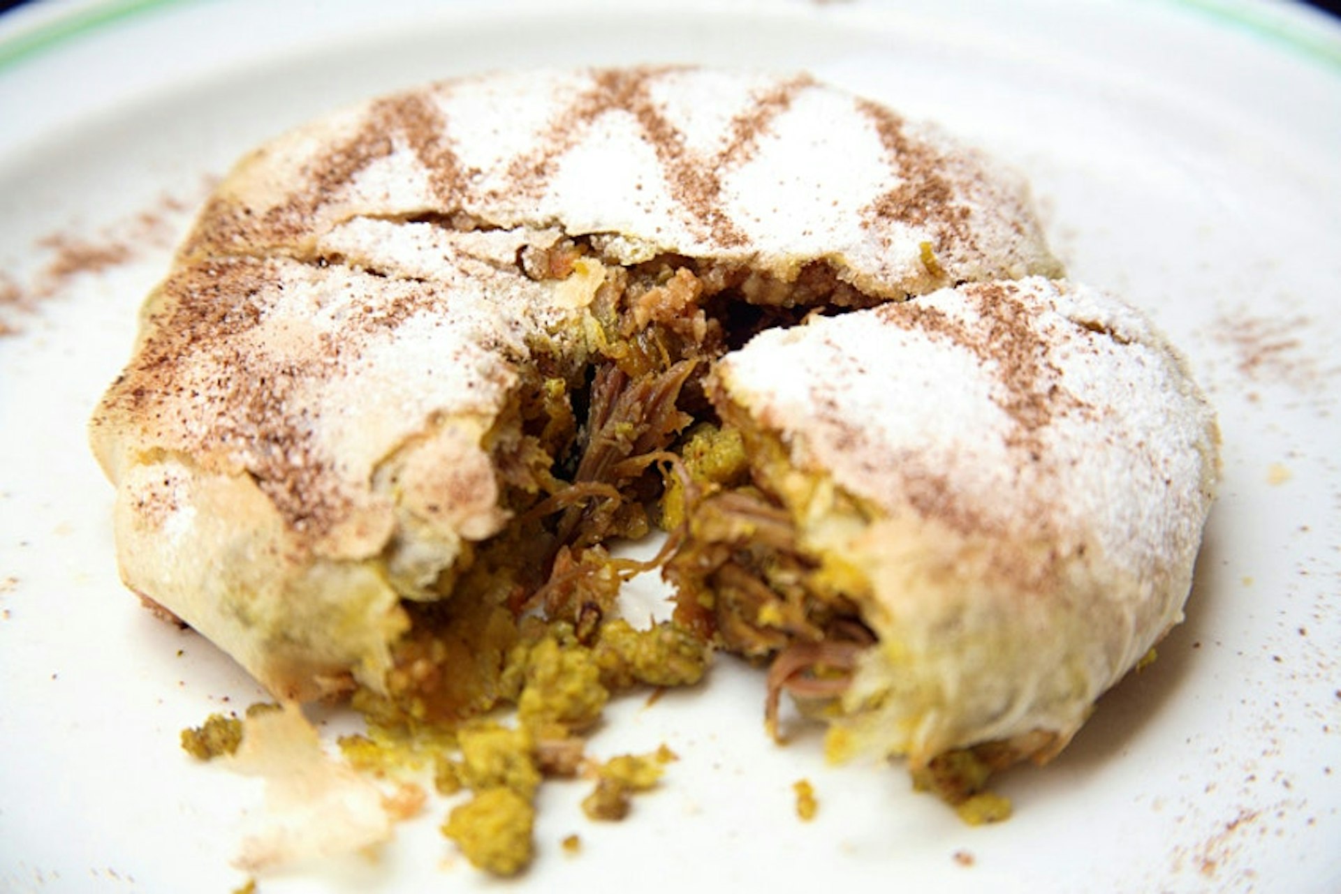 Closeup of a pastry filled with pigeon, ground almonds and topped with a layer of spices 