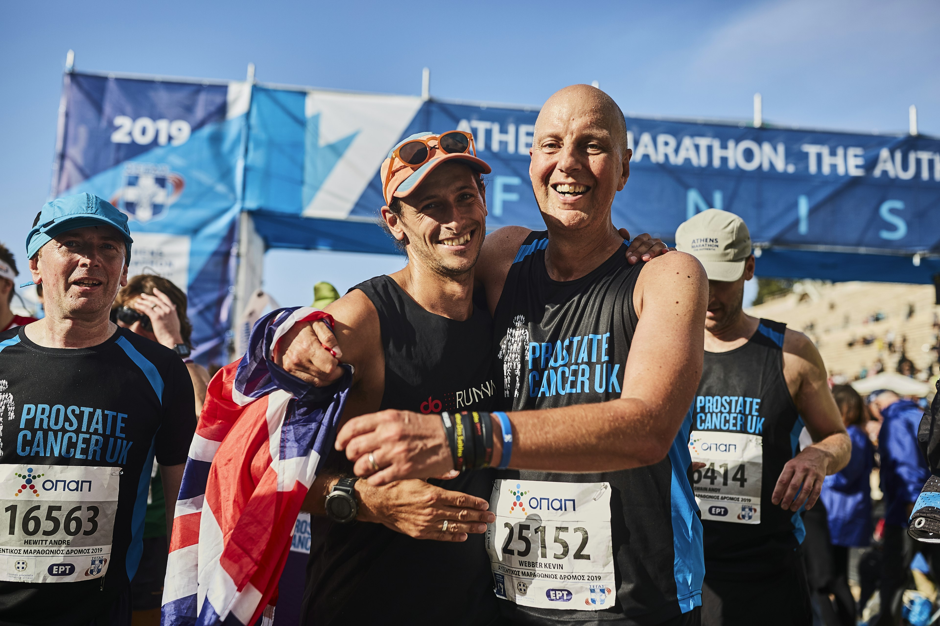 Two men embrace at a finish line reading