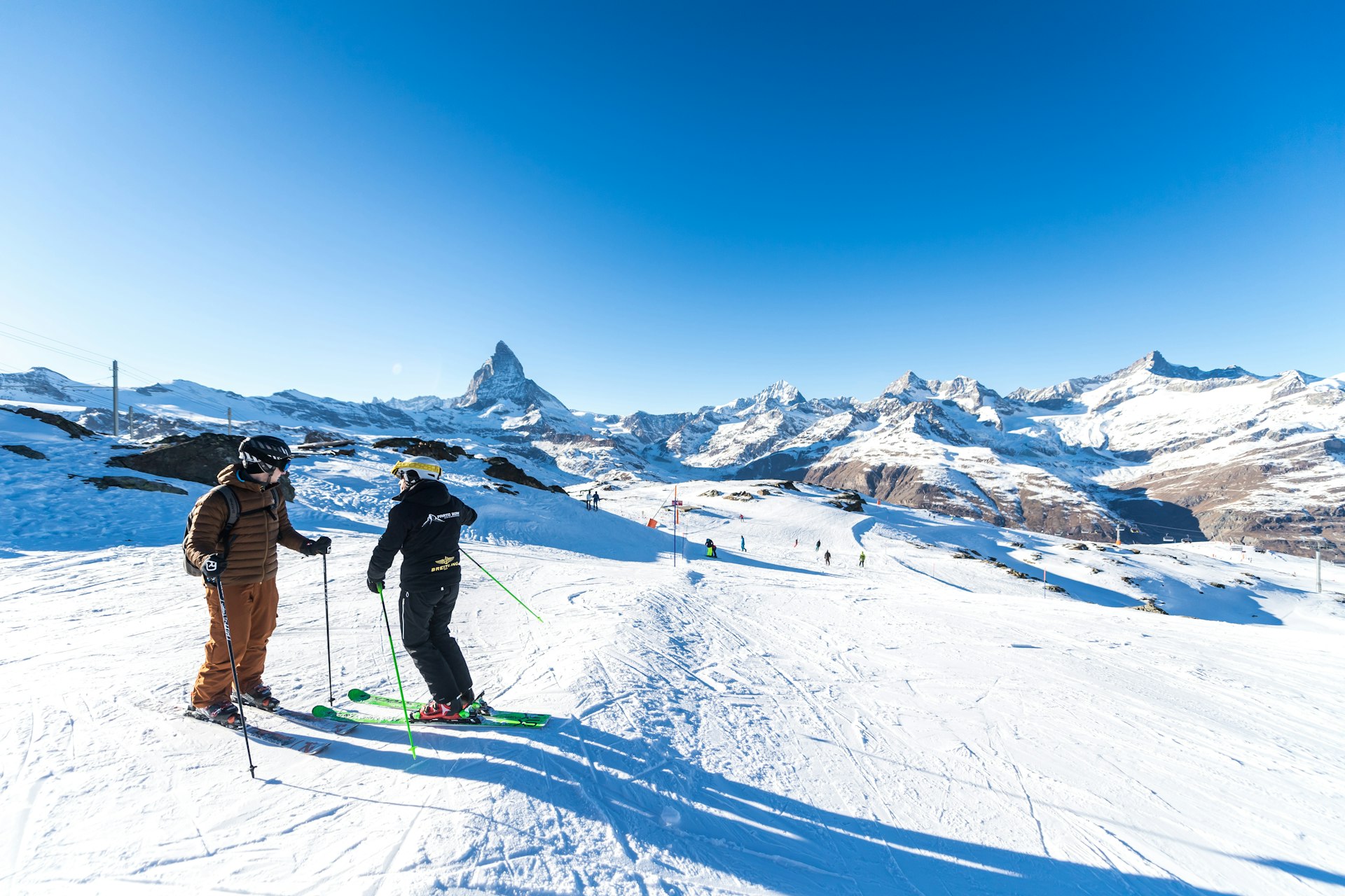 An instructor speaks to a skier as they stand at the top of a slope.
