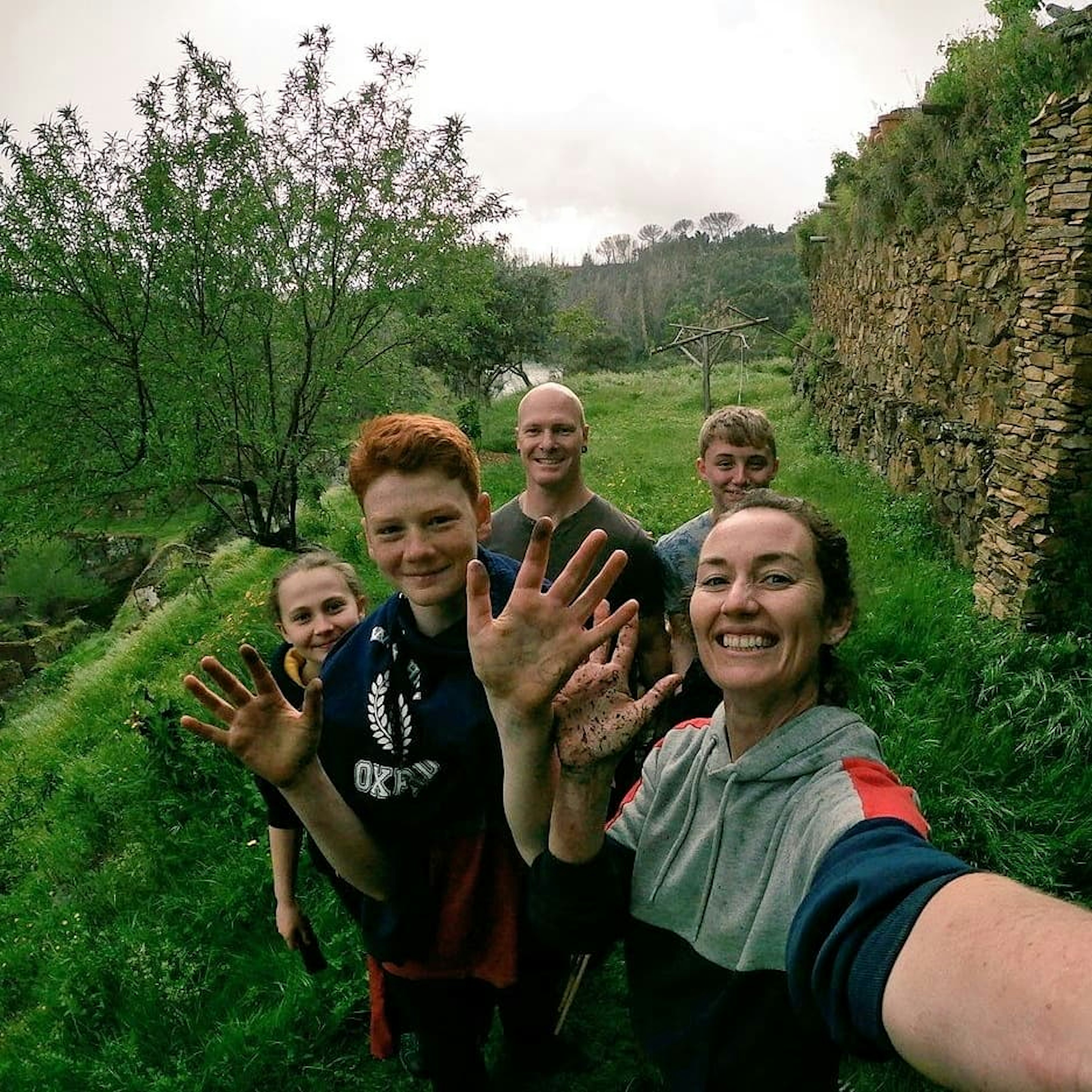 A selfie of a smiling family of five. Each one is holding up their hands, which are covered in soil from working the farmland