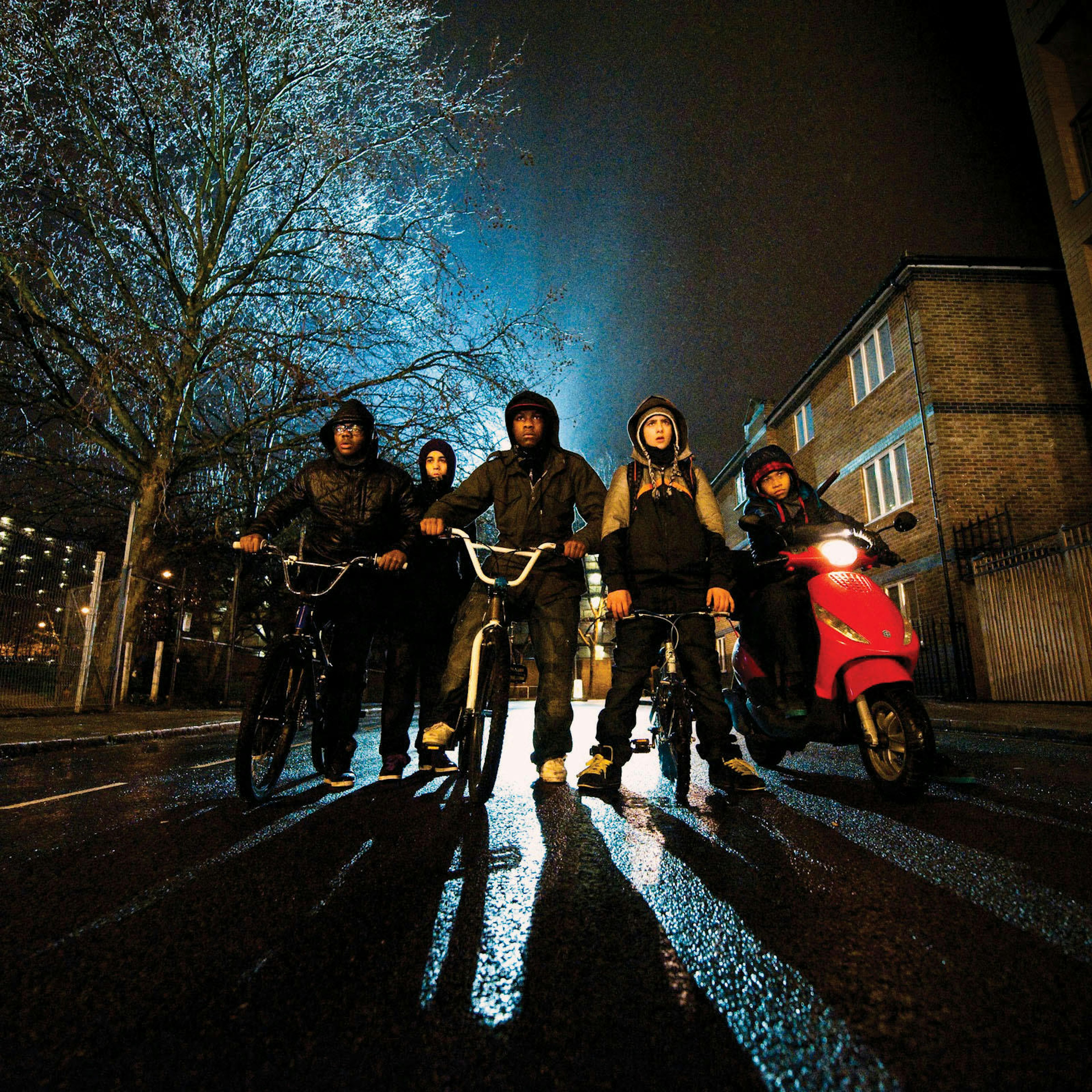 The young cast of the movie stand in the middle of a street at night, a street illuminating them from behind.