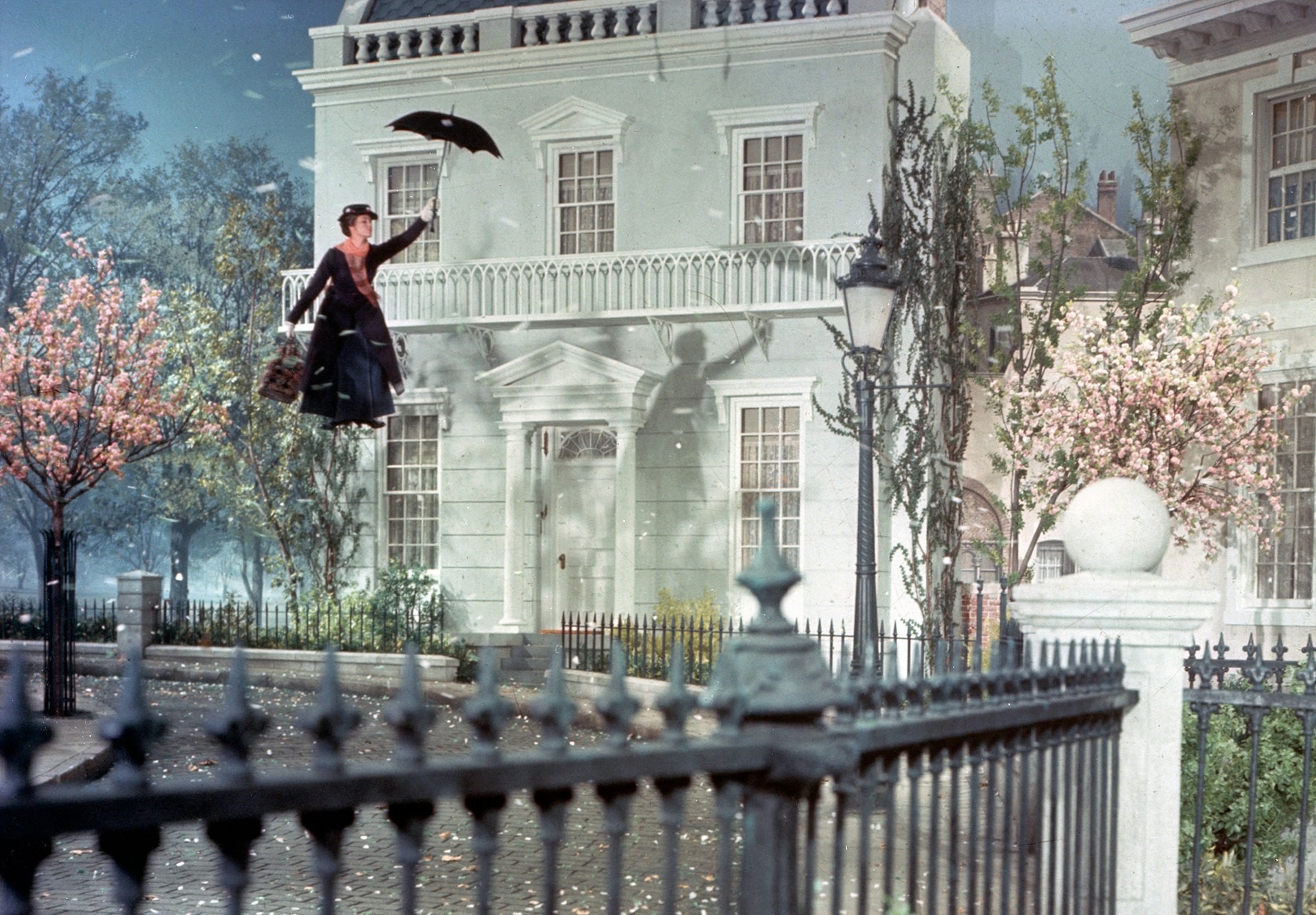 Actress JULIE ANDREWS as Mary Poppins floats down towards townhouses using her umbrella.