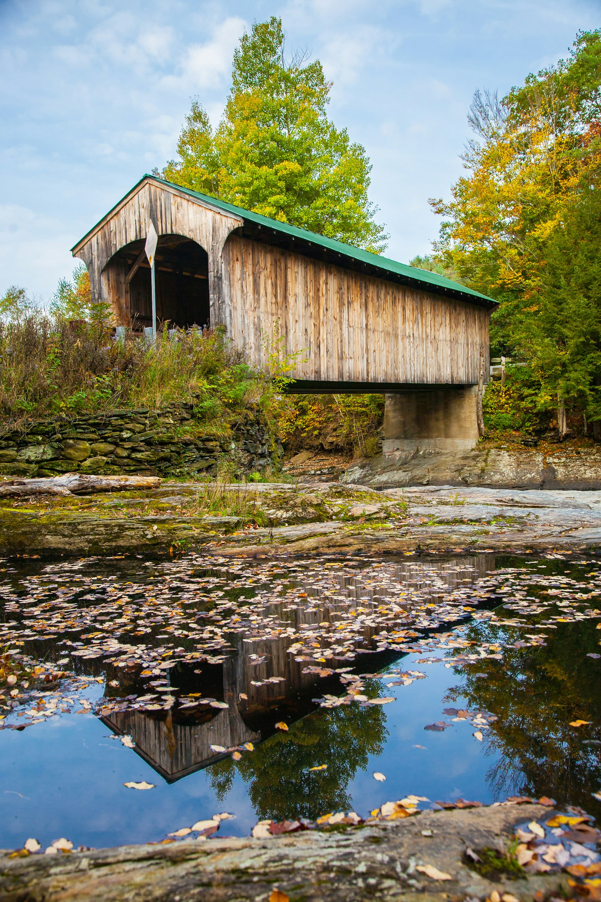 A wooden covered bridge above a leaf-covered body of water in Montgomery, Vermont
