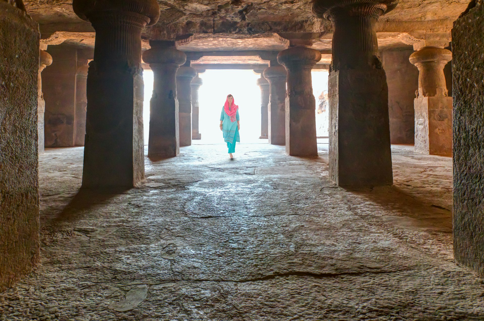 A woman wearing clothes that cover her head, shoulders and down to her ankles, walks through a temple building