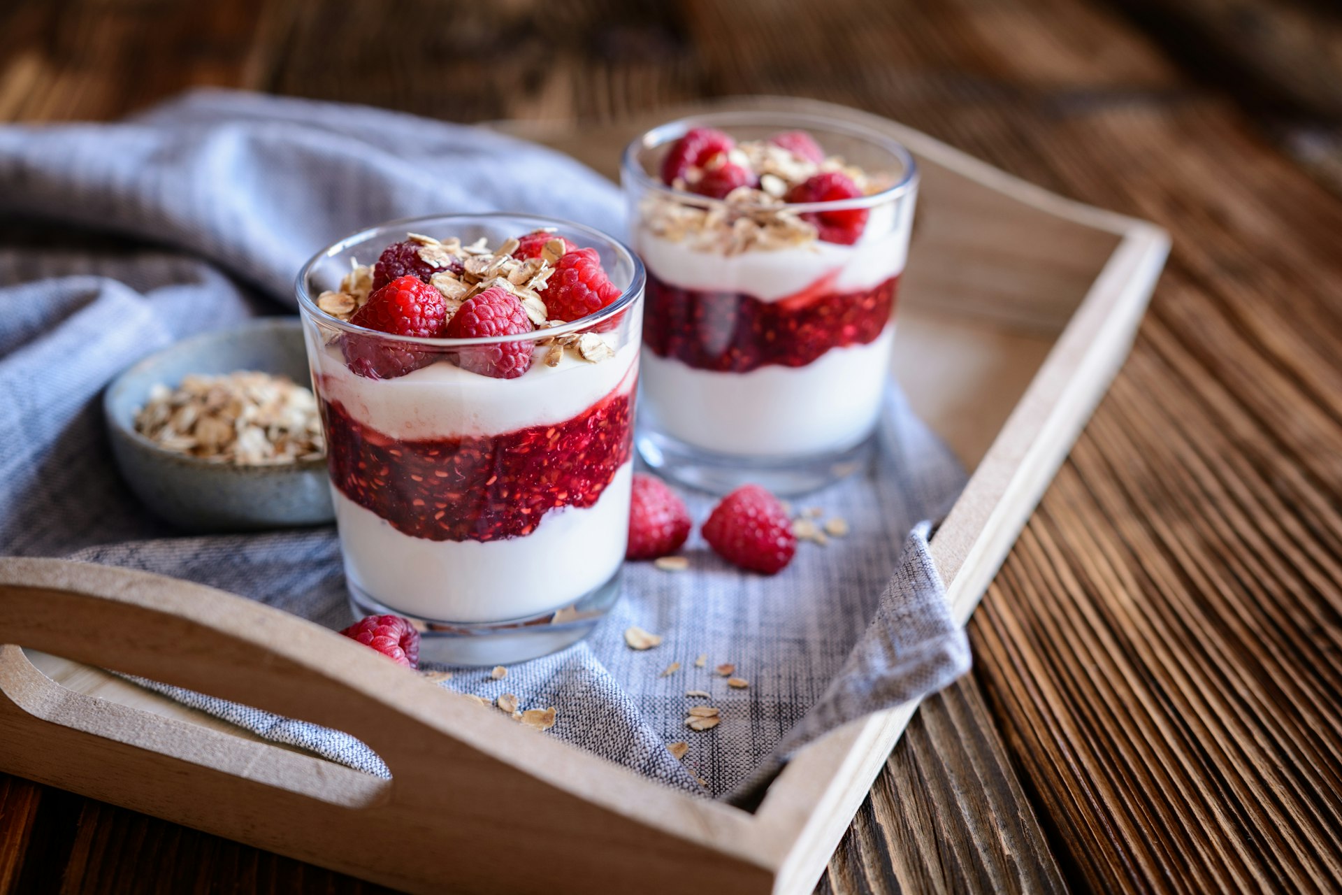 A pair of short glasses layered with whipped cream, roasted oatmeal and raspberries. The dessert is topped with strawberries. 
