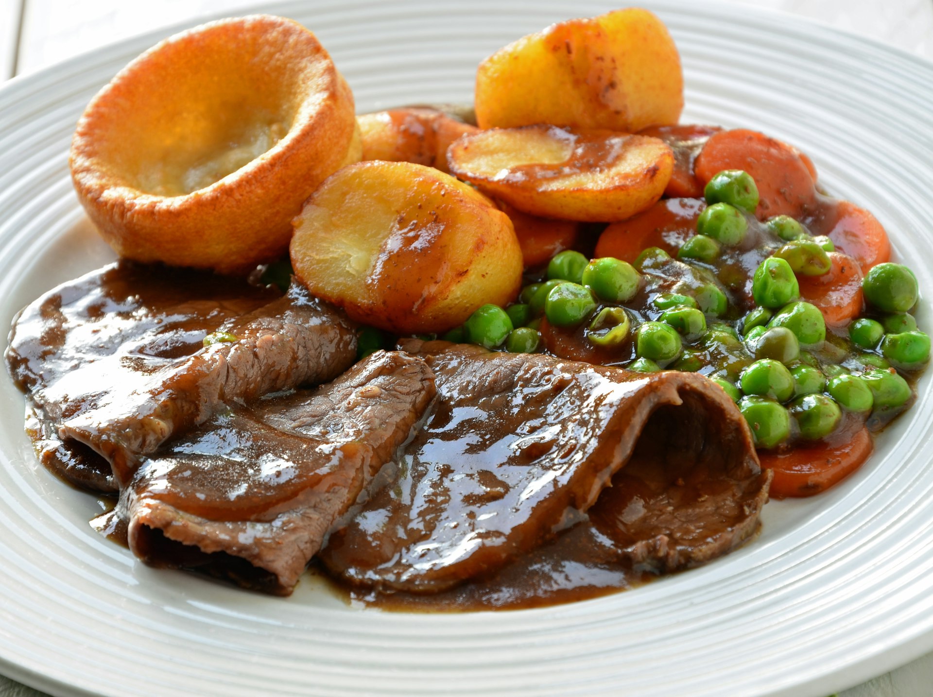 A plate of roast beef smothered in gravy with a side of Yorkshire Pudding and veggies