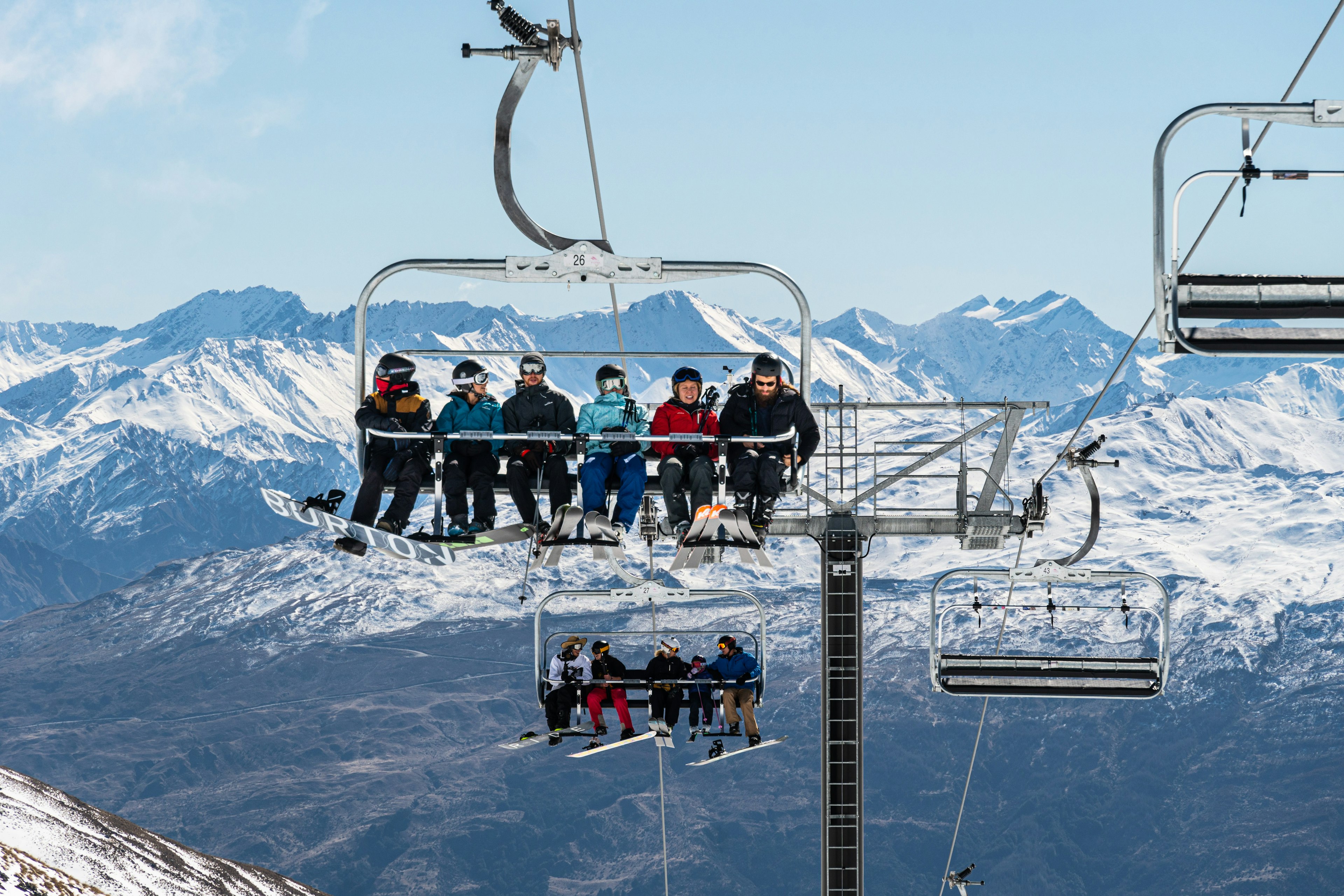 Skier and snowboarder ride a chairlift in the Remarkables ski resort in New Zealand