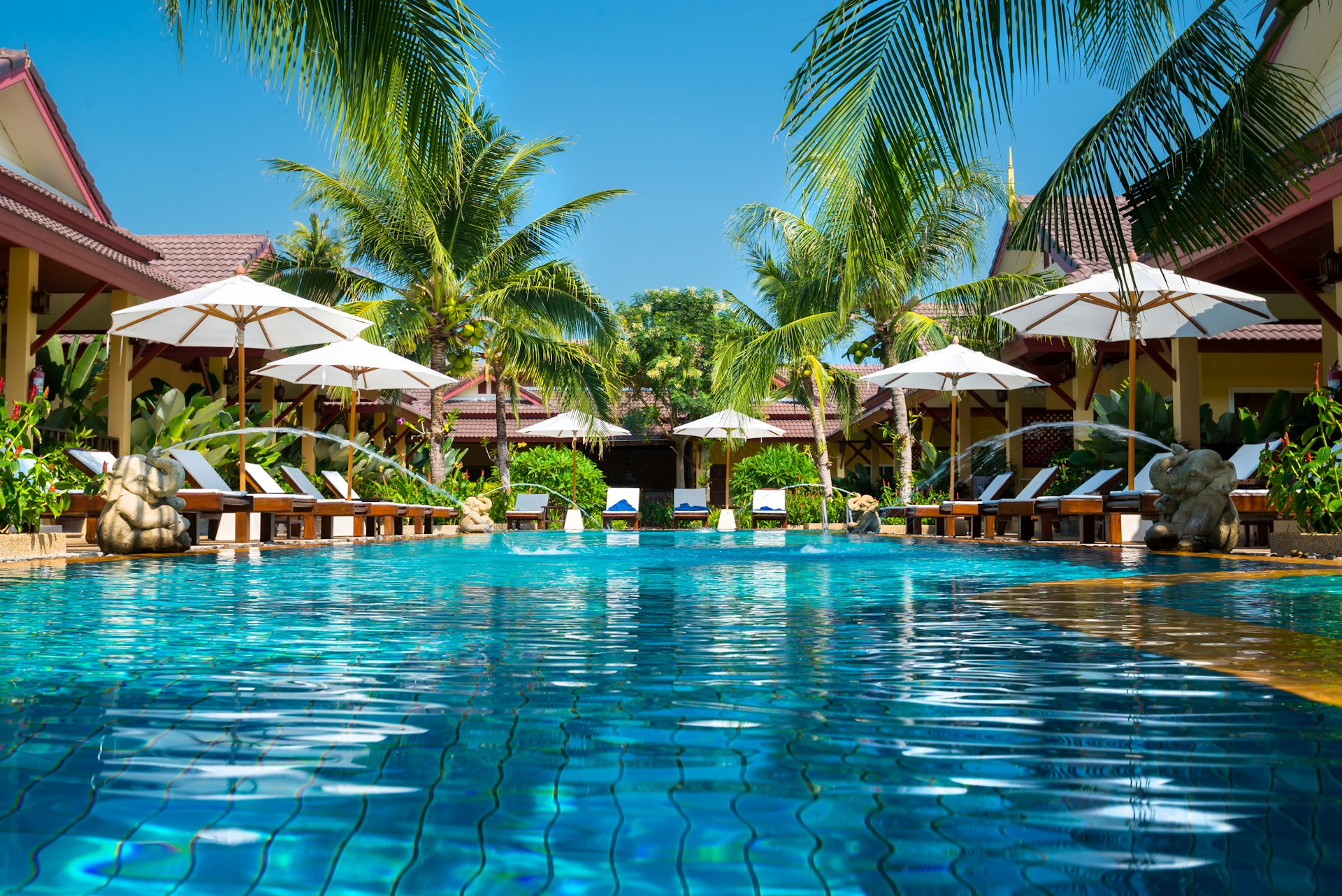 A beautiful swimming pool is surrounded by cabanas at a tropical resort. 