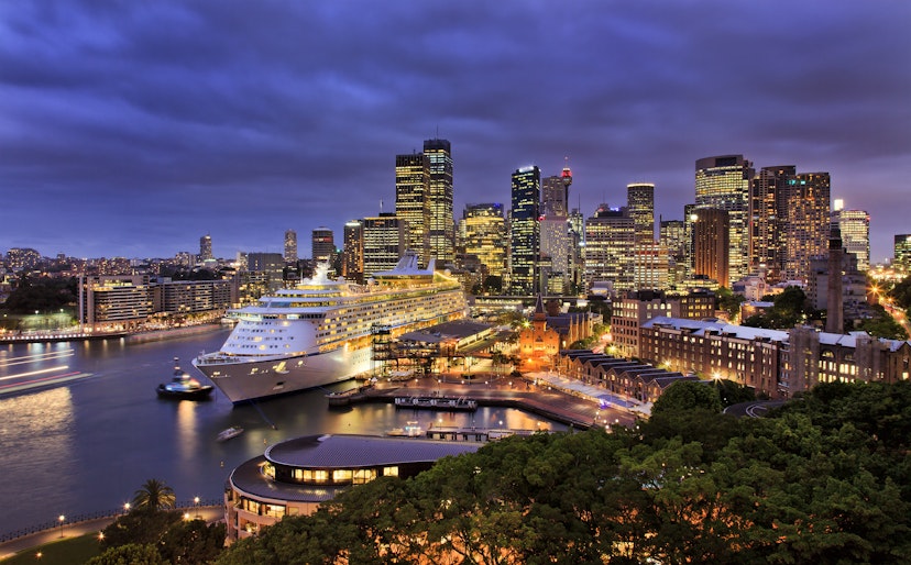 A giant cruise ship docked at Sydney harbour with the city skyline at night.