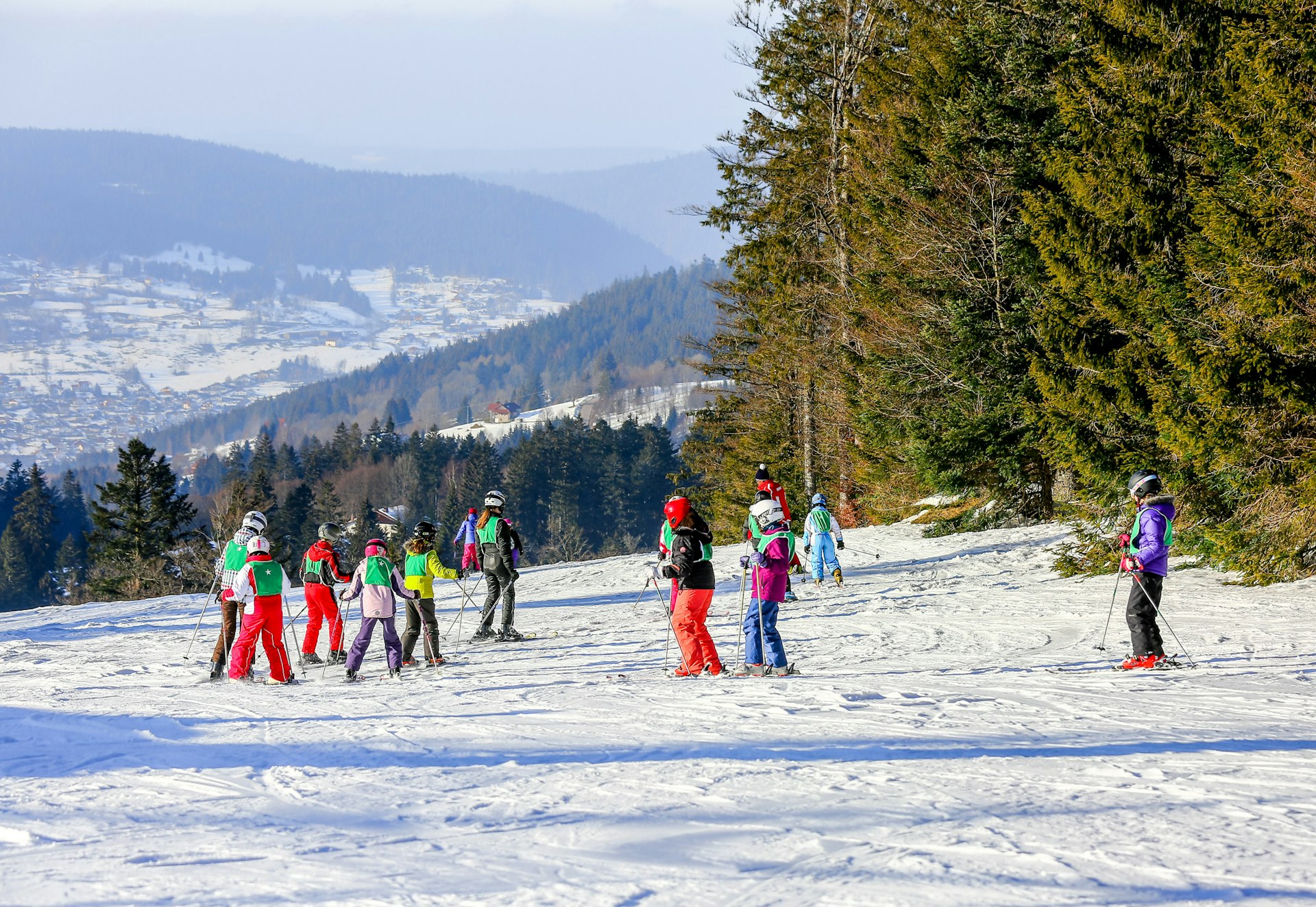 A group of children in full ski gear are led out by an instructor on the snow-covered slopes