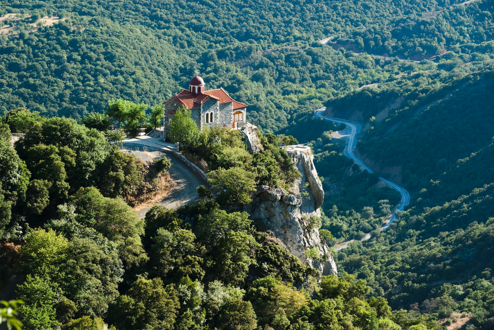 A river winding through a lush green valley with an ancient red-roofed church on clifftop