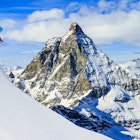 Skier skiing downhill in high mountains in fresh powder snow. Snow mountain range with Matterhorn in background. Zermatt Alps region Switzerland.