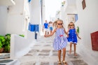 Parents and two young girls walk down stairs between white buildings on Mykonos Island.