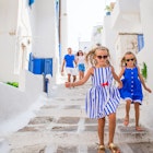 Parents and two young girls walk down stairs between white buildings on Mykonos Island.