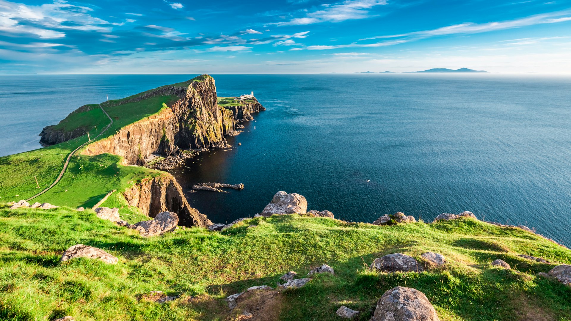 A peninsula jutting out to sea with a tiny white lighthouse at the tip. The landscape is green and completely empty of people