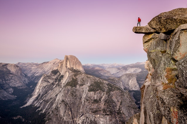 A male hiker standing on the edge of an overhanging rock at Glacier Point during twilight.
