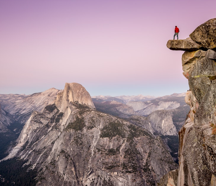 A male hiker standing on the edge of an overhanging rock at Glacier Point during twilight.