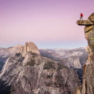 A male hiker standing on the edge of an overhanging rock at Glacier Point during twilight.