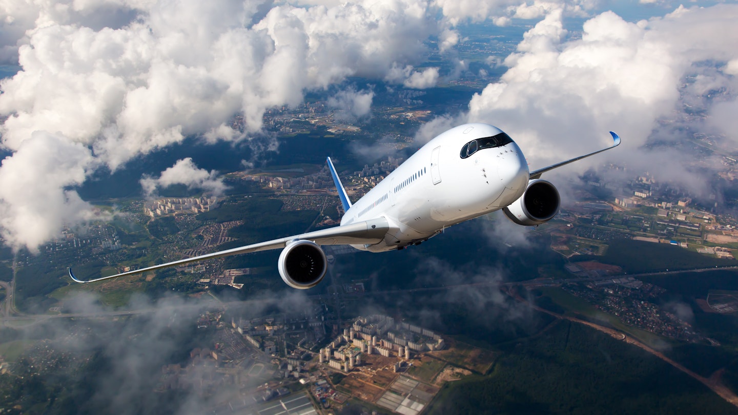 White passenger plane climbs through the clouds above a city.