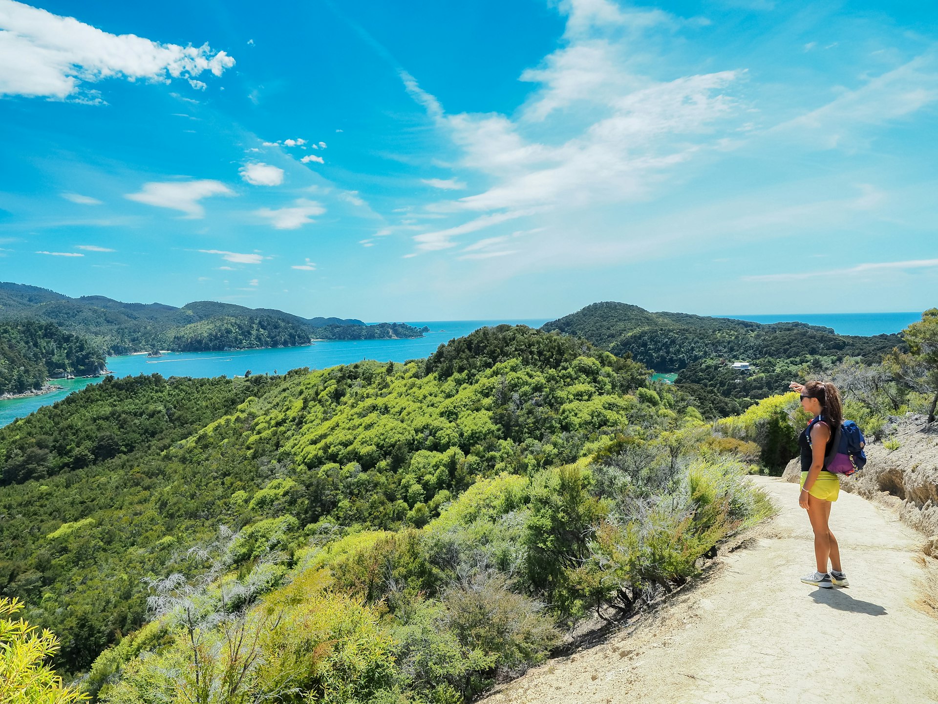 A woman stops to take in the view of the Anchorage section on the Abel Tasman Coast Track with its verdant green bushes and sparkling blue waters