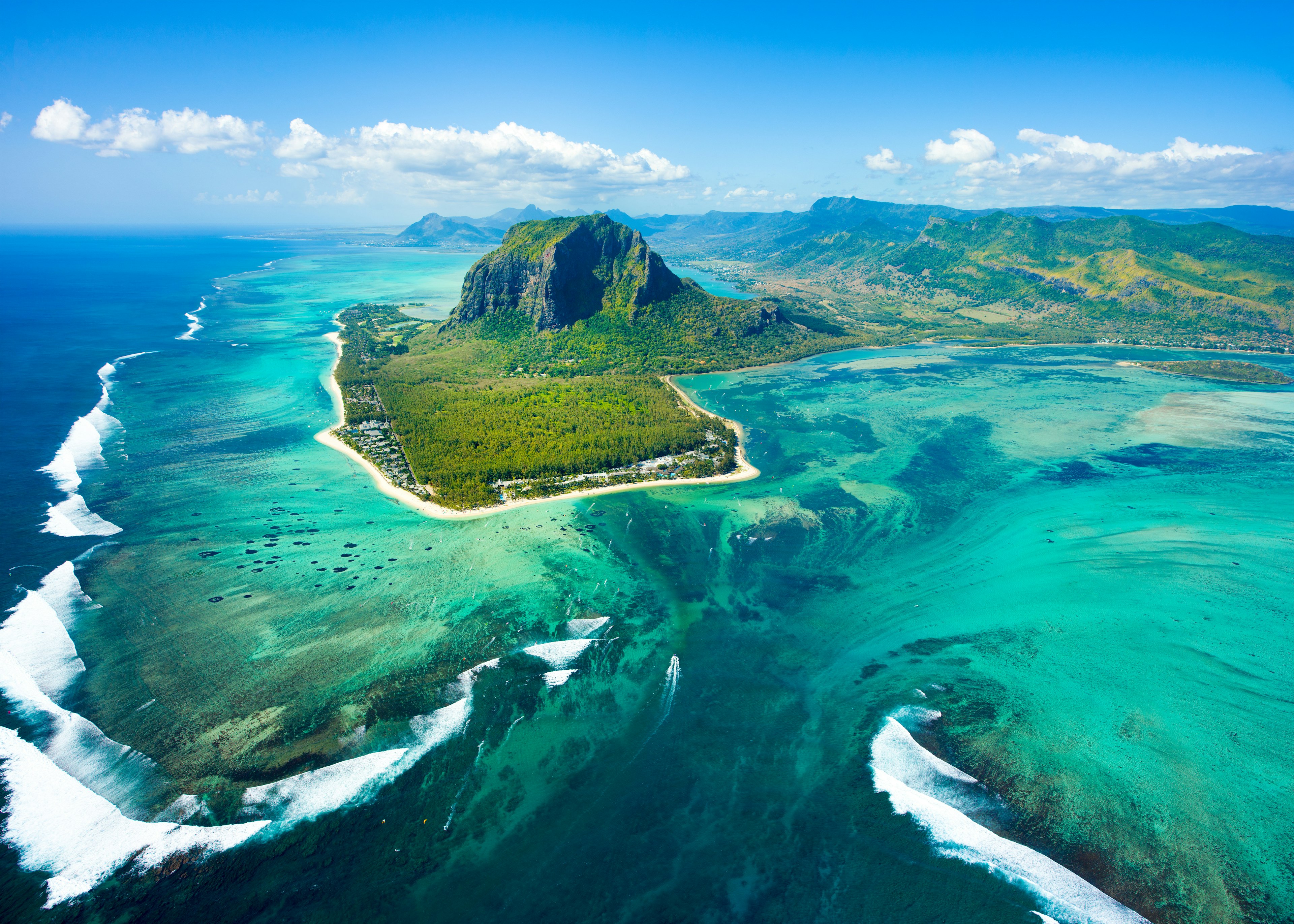 An aerial view shows a beautiful blue coastline and lush green mountain.