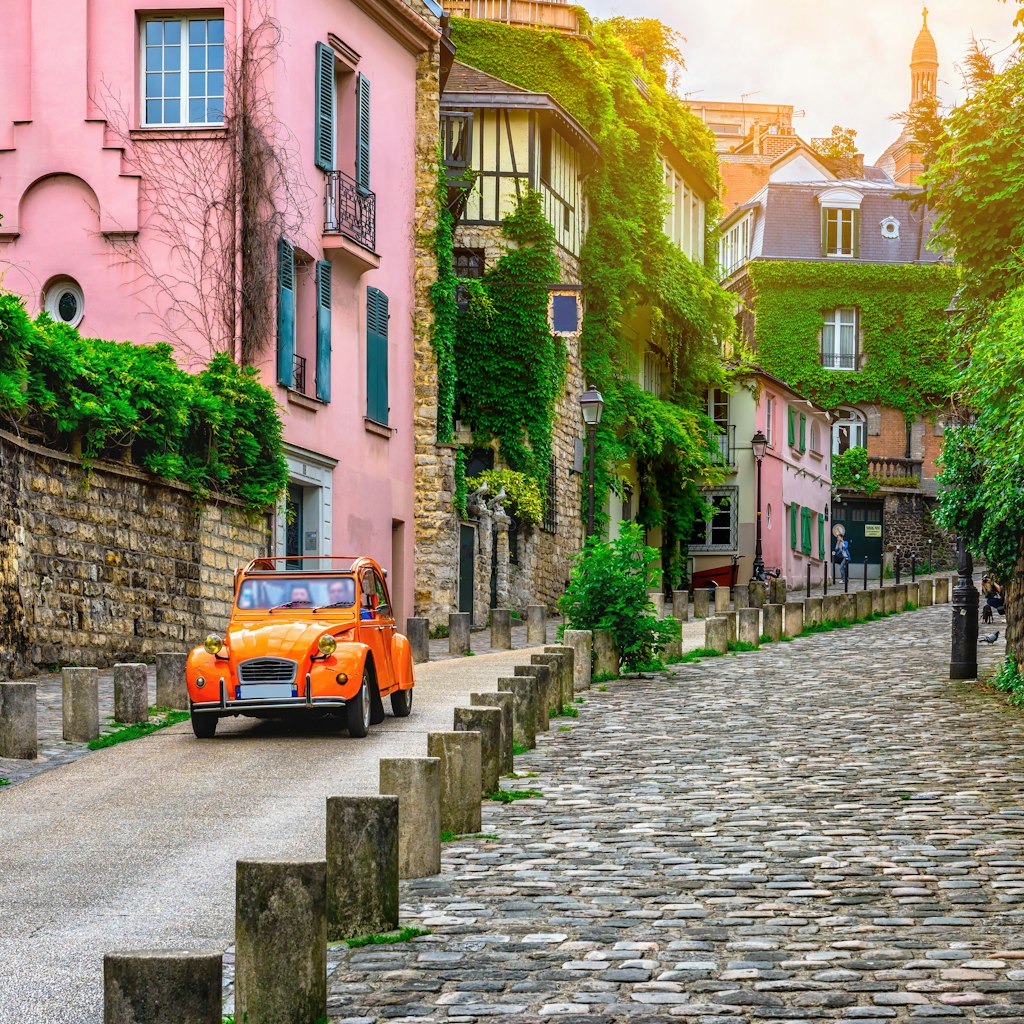 A Citroën 2CV car travels down an old street in the Montmartre quarter of Paris.