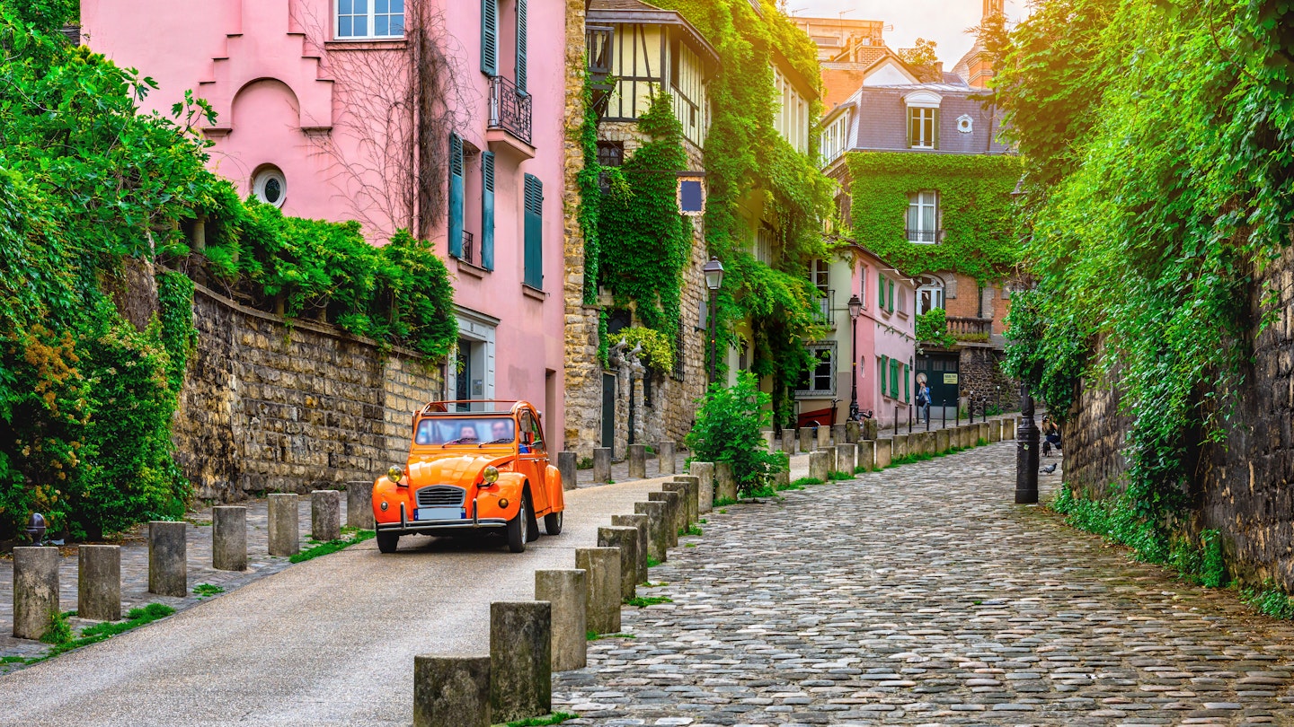 A Citroën 2CV car travels down an old street in the Montmartre quarter of Paris.