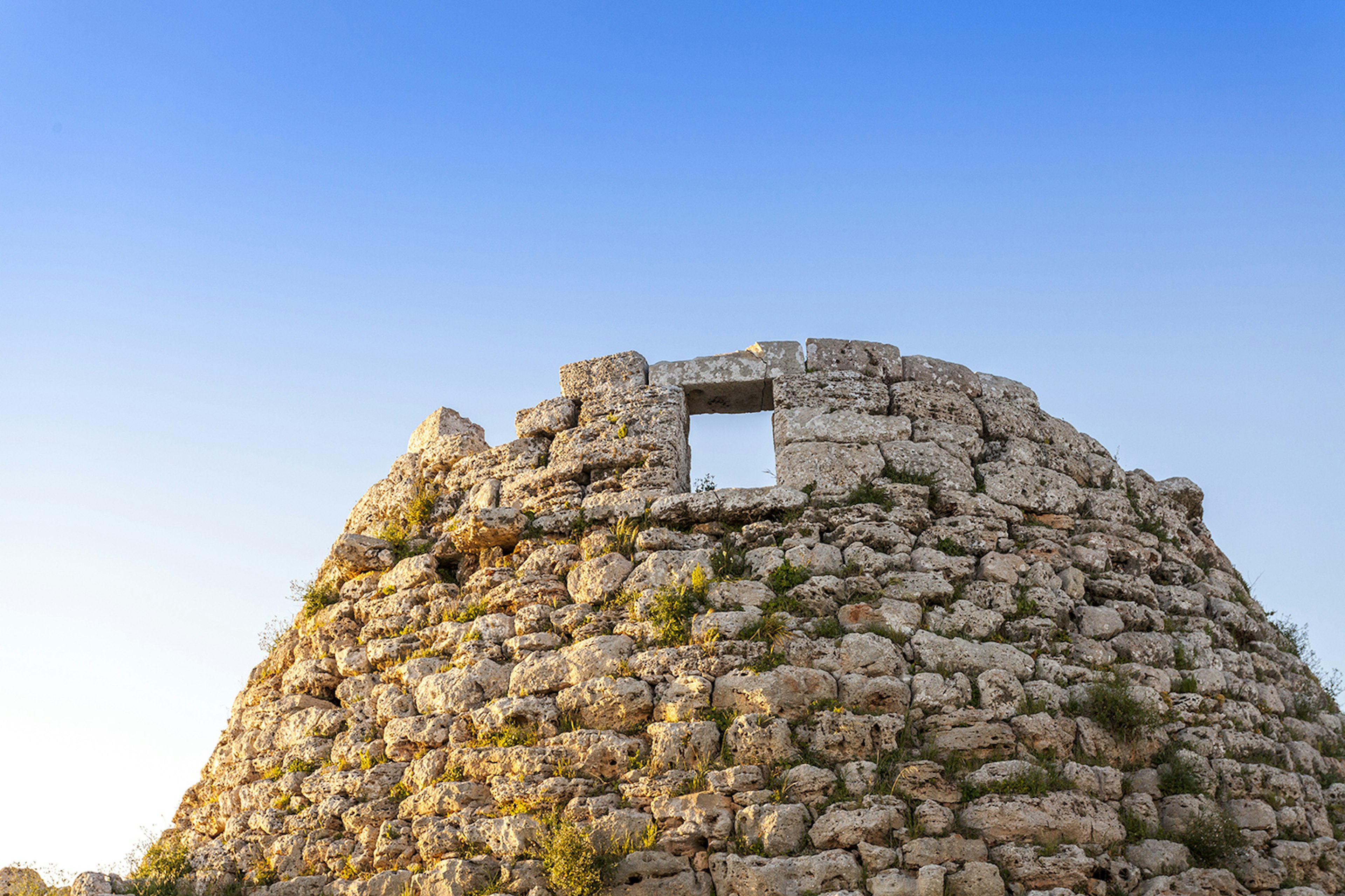 A round ancient stone hive-shaped structure formed of light colored rocks