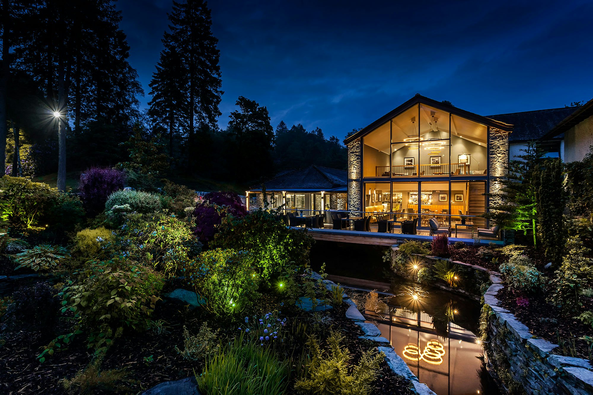 A glass-fronted lodge stands on the side of a small stream in pristine grounds