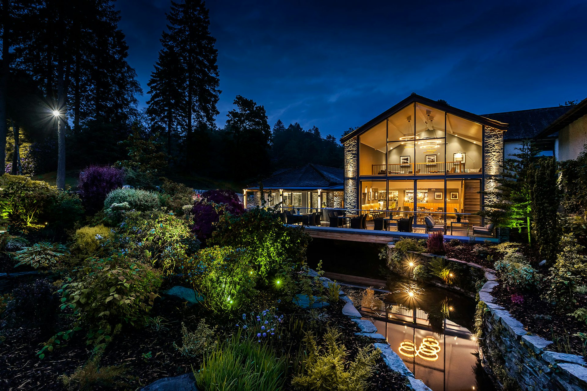 A glass-fronted lodge stands on the side of a small stream in pristine grounds