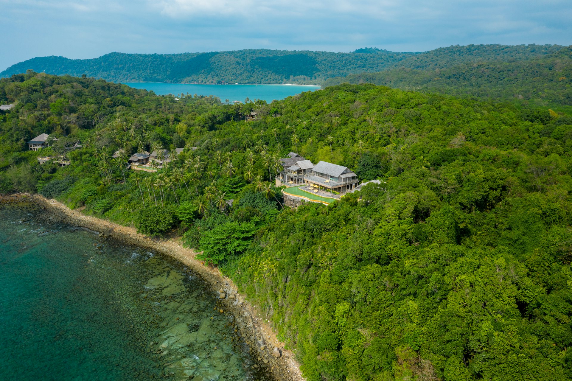 An aerial shot of a wooden lodge built on a peninsula surrounded by lush jungle