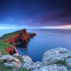 The rocky cliffs at Neist Point catching the late evening light during sunset, with the lighthouse in the distance.