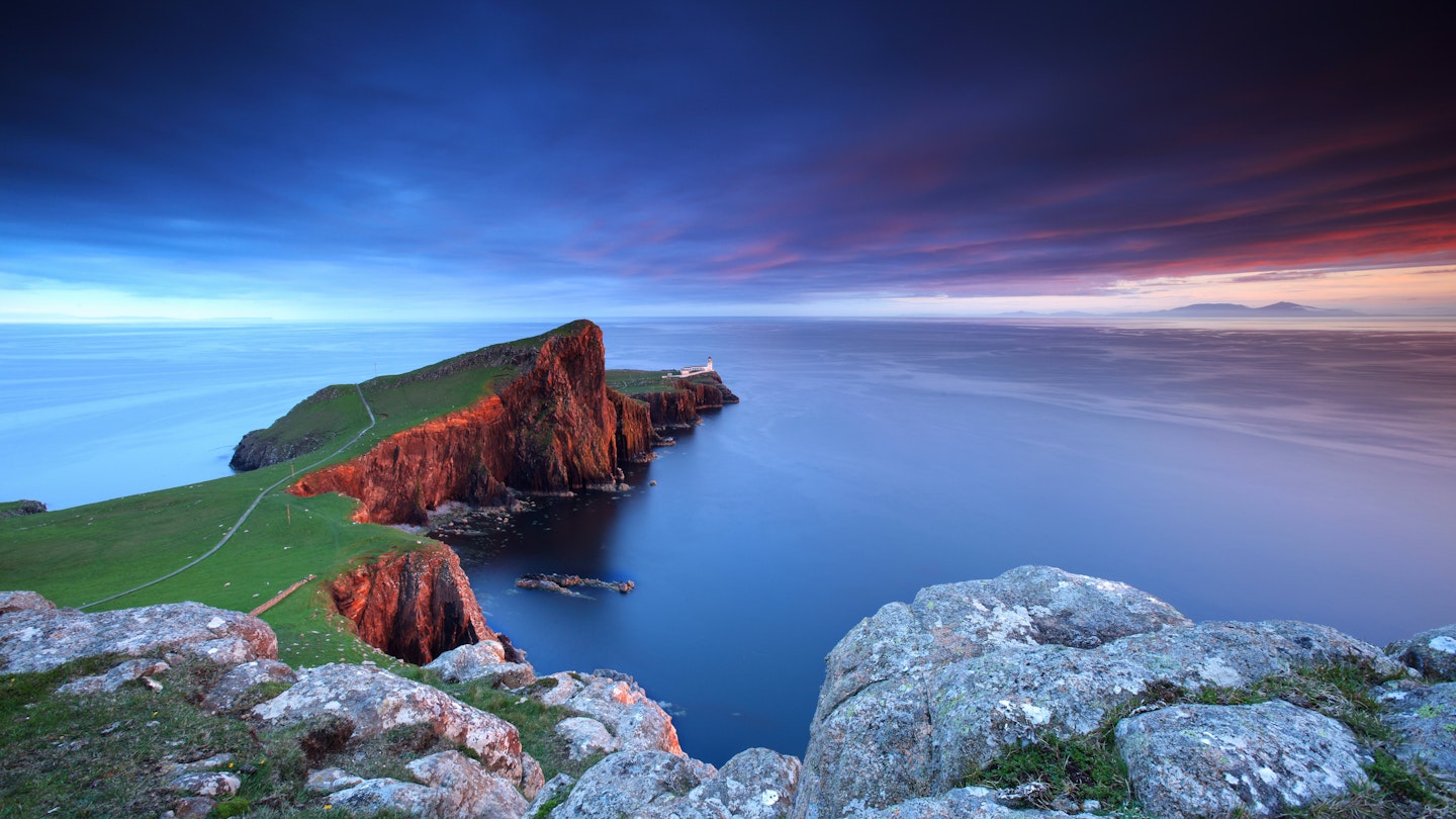 The rocky cliffs at Neist Point catching the late evening light during sunset, with the lighthouse in the distance.