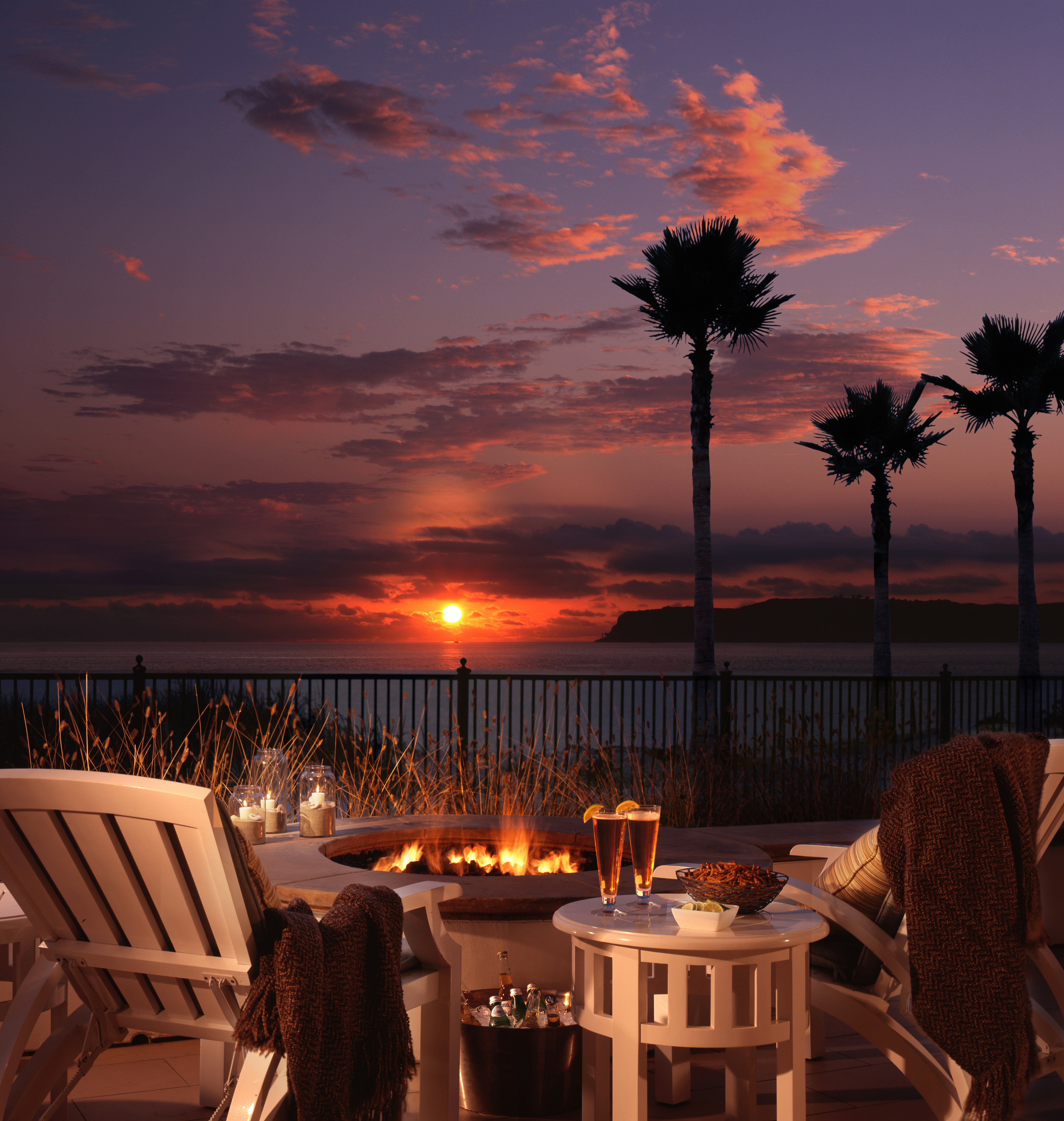 Sunset over the sea, viewed from a deck with a fire pit and two glasses of wine