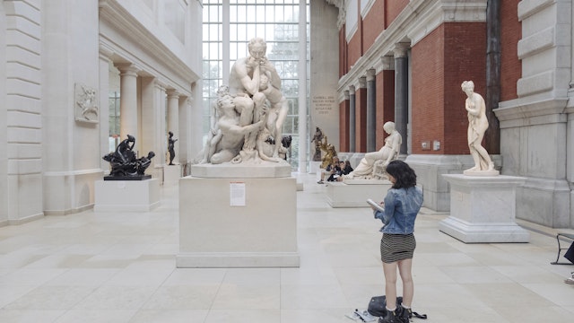 A woman takes notes in front of a sculpture at The Metropolitan Museum of Art.