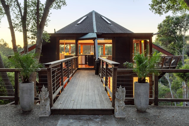 A wooden walkway leads to the entrance of a tree house with an ocean view in Aptos, California
