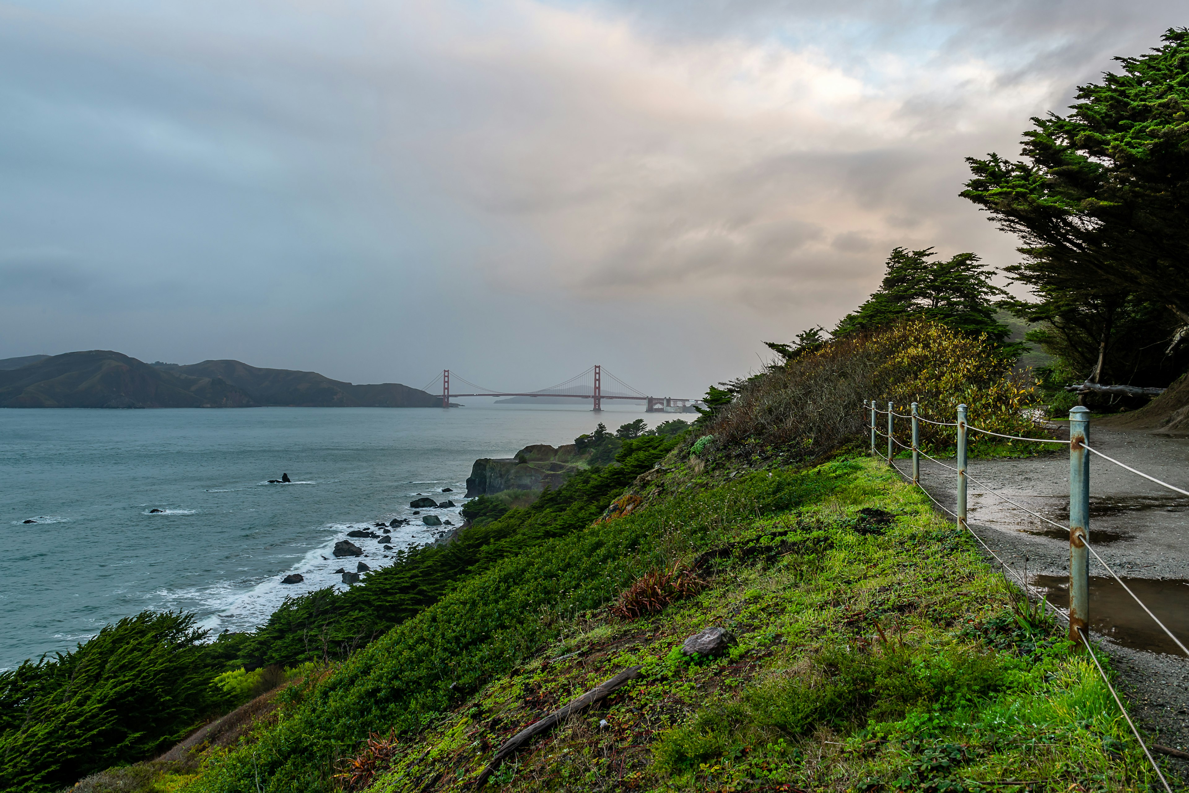 The Lands End Labyrinth and the Coastal Trail following along the San Francisco coastline towards a mist-covered Golden Gate Bridge.