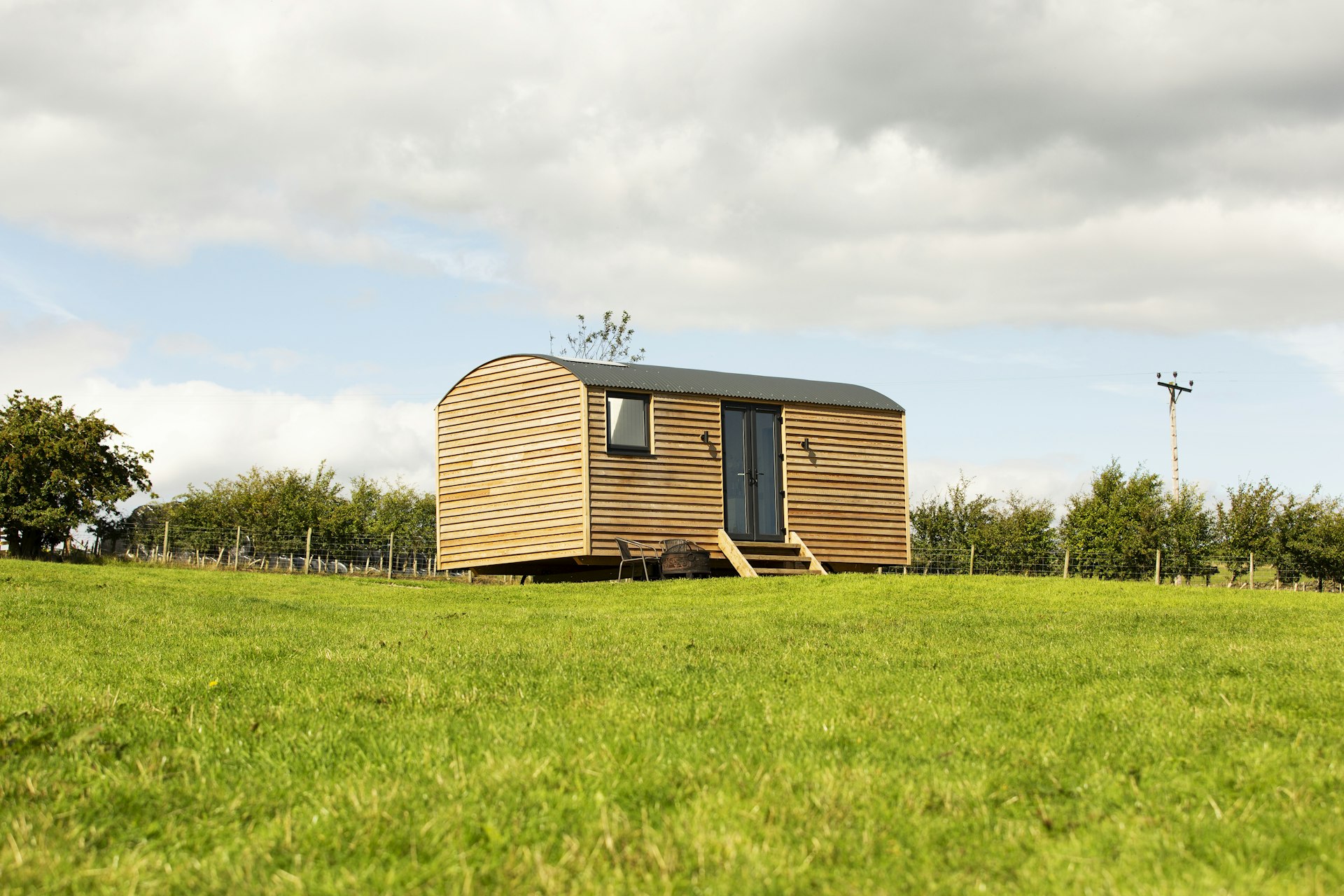 A modern wooden hut stands alone in a green field