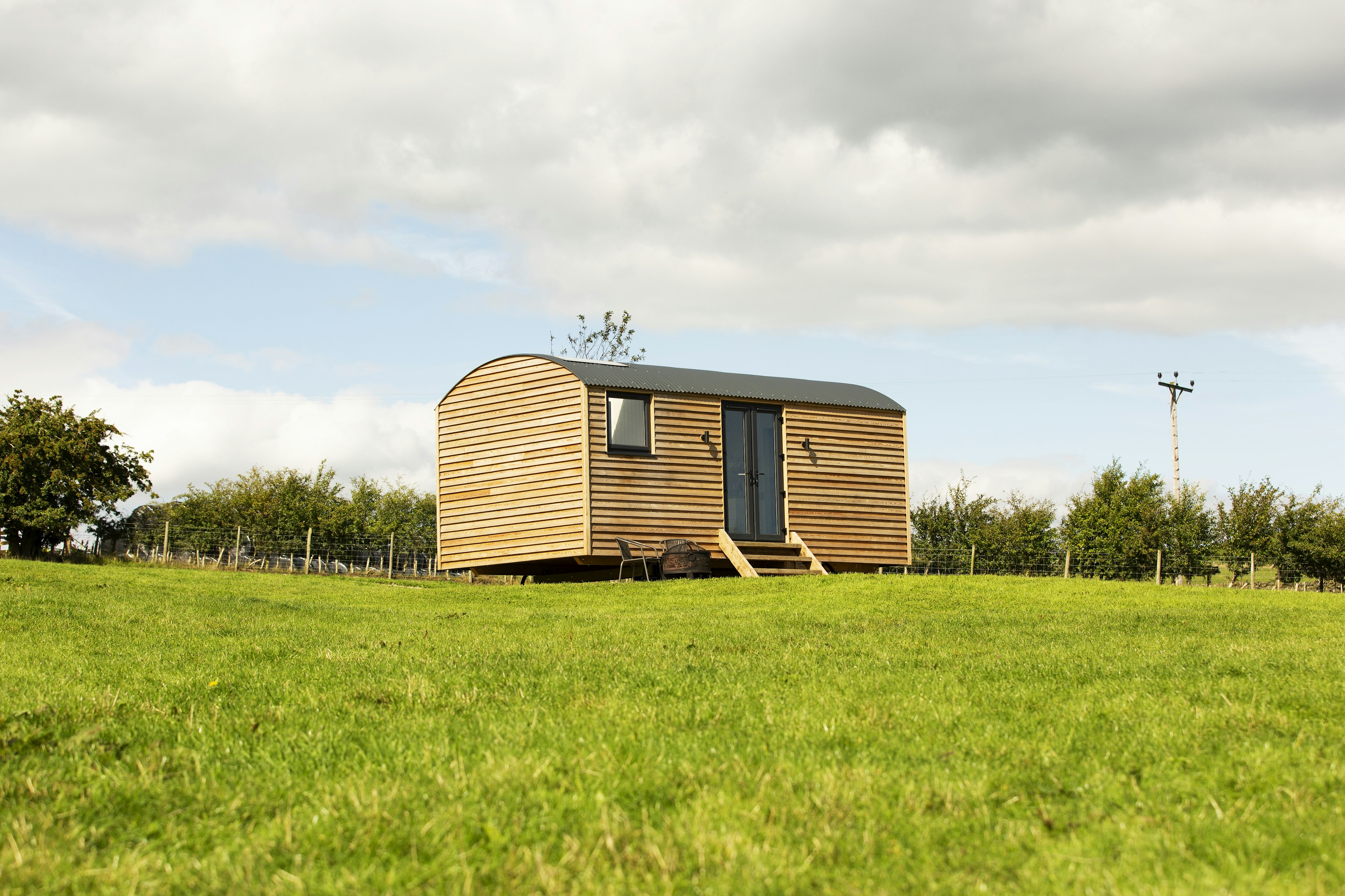 A modern wooden hut stands alone in a green field